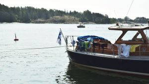 Skärgården kan locka mer än tidigare nu. En trämotorbåt fast i bojen i en gästhamn med kläder hängande på tork runt relingen. Solen skiner och i bakgrunden kör en mindre, öppen motorbåt.