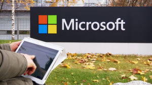 Microsoftin logo, jonka edessä tablettia pitelevä käsi.