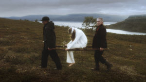 En scen ur dokumentären "Pohjolan enkeli". Två gossar bär en bår där en sårad, vit ängel sitter. Fotot återskapar Hugo Simbergs målning "Sårad ängel".