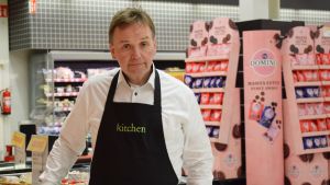 Hannu Aaltonen säger att det finns andra fördelar med nattöppet än att försäljningen skulle vara stor. Hannu Aaltonen iförd vit skjorta och svart förkläde inne i matbutiken, mathyllor syns i bakgrunden.