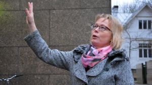 Sanna Simonen säger att det finns planer för att förbättra stadshusets hälsa. Sanna Simonen står vid ett hus och pekar upp mot taket.