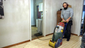 Mufid Azad har haft eget byggföretag i två år. En skäggig man slipar ett golv.