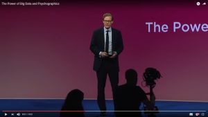 Alexander Nix föreläser om sitt företag Cambridge Analytica som nu också ger sig in på konsumentmarknaden. Skärmdump av en Youtubevideo där Alexander Nix håller föredrag i kostym och glasögon med tv-bågar.
