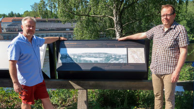 Porträtt av Kim Björklund och Aapo Roselius vid en skylt med ett gammalt fotografi av Billnäs.