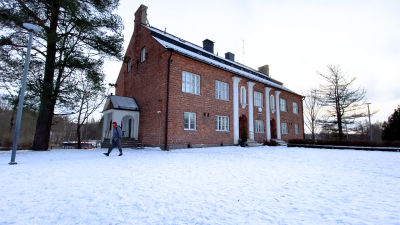 En stor tegelbyggnad, med snöig gård. En person går framför byggnaden.