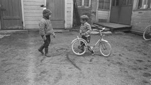 Lapset leikkivät pihalla. Kaksi lasta ja polkupyörä.