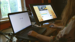 Nainen istuu kahden tietokoneen edessä, joilla auki Google ja Huuto.net.