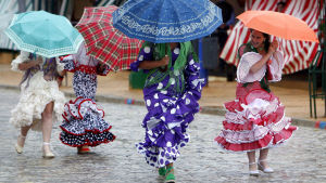 Flamencoasuiset naiset rientävät sateenvarjojen alla feria-alueella Sevillassa.