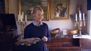 Maria Sjöblom visar upp en broderad kudde för eleverna. Kvinna står i muséum med dyna i handen.