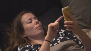 nainen makaa sängyllä ja katsoo älypuhelinta