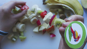 Leikkuulaudalla on pilkottuja hedelmiä, ja käsissä on varrastikkuun tökättyjä hedelmäpaloja.