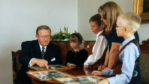 Martti Ahtisaari katgselee valokuvia Linnassa vierailevien lasten kanssa.