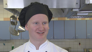 Andreas Tallberg är nöjd med den praktik han har fått under studietiden, trots att han studerar enligt det gamla yrkesutbildningssystemet. Ung kockstuderande man i kockmössa i undervisningskök.