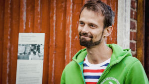 Det är kul att huset man bor i har en historia, säger Anders Jungar. Vanhan Malmin asukas Anders Jungar kuvattuna punaisen puutalon edustalla, päällä vihreä huppari, raidallinen t-paita
