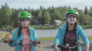 Daniela Back och Erika Nybo bor i Södra Vallgrund. De gillar närheten till stranden och vattnet speciellt mycket. Två flickor med varsin grön cykelhjälm på huvudet lutar mot sina cyklar.