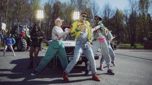 Tanssijat Antti Tuiskun Kesäkumibiisinvideon kuvauksissa koripallokentällä, taustalla auto ja traktori