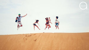 Perhe seisoo hiekkadyynin päällä ja hyppää ilmaan.