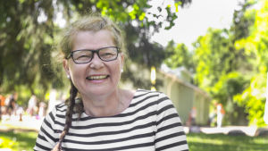 - Jag trivs verkligen bra med det här jobbet, säger Anneli Bäckström, som jobbar i lekparken Intia i Forsby i Helsingfors. Anneli Bäckström från axlarna uppåt, sitter på en gräsmatta i lekparken Intia i Forsby i Helsingfors.