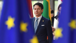 Italiens premiärminister Guiseppe Conte i bakgrunden, EU-flaggor i förgrunden.