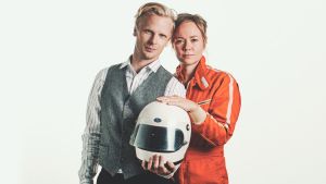 Joppe Dikert iklädd formulaoverall med sin man Oskar Pöysti i famnen. Han har en formel1- hjälm i famnen och en champagneflaska i handen. De ser ivriga och glada ut.