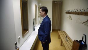 Ulf Kristersson. Ulf Kristersson, klädd i mörkblå kostym, är fotograferad i profil där han står i ett omklädningsrum och tittar in i en spegel.