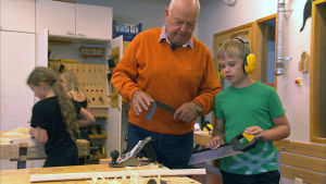 Medfostrare Göran Snellman tillsammans med Alexander Rosenberg i Gerby skola. Äldre person tillsammans med en pojke med hörlurar på och såg i handen.