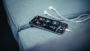 Suositulle soittolistalle pääseminen vaikeutunee etenkin tuntemattomampien artistien kohdalla. Puhelin sohvalla, Spotify-soittolistavalikko näytöllä.