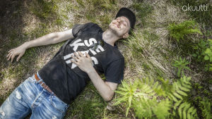Mikko Toiviainen makaa selällään metsässä ja hymyilee silmät kiinni.