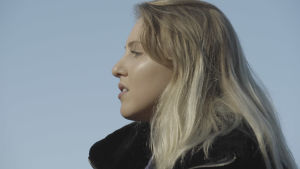 Molly fick aldrig tid för att vila. En kvinna med långt blont hår. Vi ser henne från sidan. Hon står och tittar åt vänster i bilden.