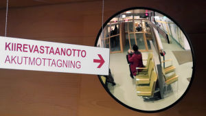 Skylt där det står akutmottagning och en spegel där en kvinna som sitter och väntar syns.