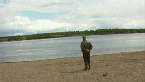 Jakaväkirykmentti 12 sotaveteraani katselee tunteikkaana järven rannalla yli veden. Selin kameraan.