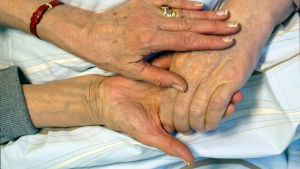 Ikääntyvä nainen koskettaa puolisonsa kättä.
