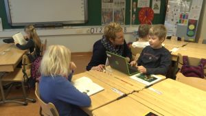 Klasslärare Susse Båge hjälper Lucas Holmström med Läsväskan. Lärare jobbar tillsammans med en elev i ett klassrum.