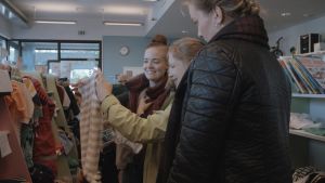 I somras kollade Milja (till vänster) och Nina Boström på kläder till babyn som föddes i december. Märta Westerlund (till höger) intervjuade dem för serien Fem fenomen inom medicin. Nina och Milja Boström tittar på babykläder. Reporter Märta Westerlund tittar på.