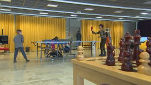 Familjen Almark-Mannila består av mamma Johanna, pappa Kaarle och deras barn som är 22, 19, 17, 15, 12 och 9 år gamla. De två yngsta undervisas fortfarande hemma. En kvinna och ett barn spelar pingis med ett schackbräde i förgrunden.