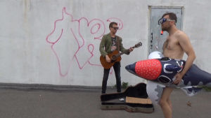 Musiktestet testar publikens kunskaper i pop och rock-trivia. Naken man skyld av badleksak promenerar förbi gatumusikant.
