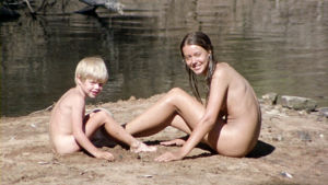 Jenny Agutter ja Luc Roeg erämaan armoilla. Nuori poika ja tyttö istuvat alasti maassa veden äärellä ja hymyilevät. Kuva Nicolas Roegin elokuvasta Walkabout.