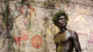 David Gulpilil. Nuori aboriginaali seisoo kalliomaalausten edessä. Kuva elokuvasta Walkabout.