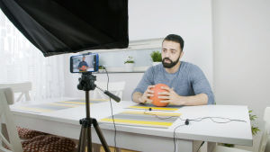 Dokumenttiprojekti: Pian hän tulee. Mies istuu pallo kädessä pöydän ääressä ja puhuu videokameralle.