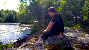 Thomas Enroth vid sommarstugan i Fagernäs, Larsmo. En oas som ger avslappning och inspiration. en man sitter på en sten vid stranden och tittar ut mot havet