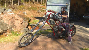 En man i långt skägg med glasögon sitter på en specialbyggd Choppermotorcykel.
