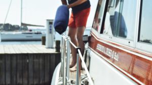 I exceptionella tider behövs gemensamt ansvar, säger man från sjöbevakningens sida. En man med orange shorts kastar över en fender över relingen.