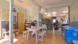 Jessica Blomqvist trivs med arbetet i Iniö lanthandel. vy över lanthandeln med bord, glassförvaring och varor och kunder i bakgrunden.