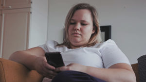 När Emma Geisor fick en panikattack så stark att hon misstog den för en hjärtinfarkt förstod hon att det var allvar. Emma Geisor sitter i sin soffa och scrollar på mobilen. Hon har en vit t-skjorta på sig.