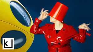 Futuro-muovitalo ja henkilö, jolla ämpäri päässä ja punainen lateksitakki