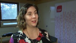 Anette Karlsson från Borgå anser att det behövs mer hjärta i beslutsfattandet. Anette Karlsson intervjuas. Hon ler och ser på personen som intervjuar henne. Bredvid henne syns SDP:s logotyp.