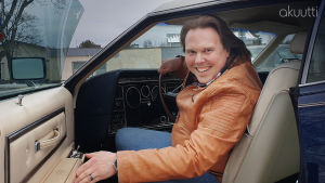 Sami Nieminen istuu autossa ja katsoo avoimen oven kautta hymyillen kameraan.