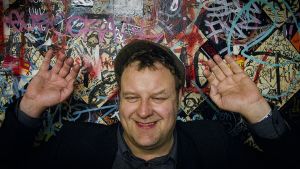 Joose Berglund kädet ylhäällä graffitiseinän edessä
