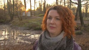 Maria Mäkinen är grundvattenexpert vid NTM-centralen. Maria Mäkinen, en dam med rött, lockat hår, står vid en uttorkad damm.