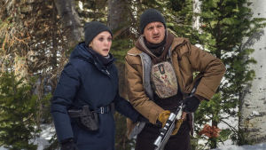 Wind River. Nainen ja mies metsässä, miehellä pyssy. Katsovat eteensä hätääntyneen näköisinä.